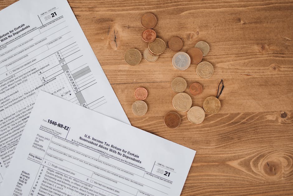 Flat lay of tax forms and scattered coins on a wooden table, illustrating finance and taxation concepts.