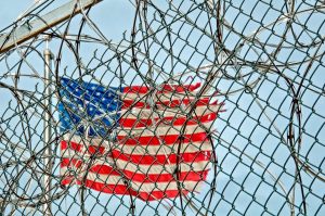 Australian deportation risks: USA flag behind barbed wire, symbolizing freedom and protection.