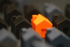 Falling house prices in Australia: Orange model house symbolizes real estate market shifts.